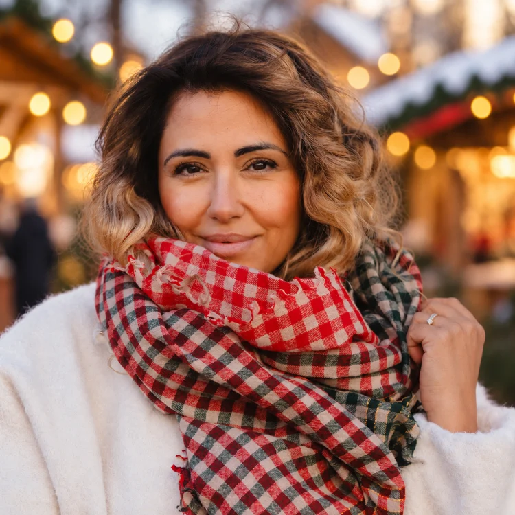 FRau mit einem dicken, karierten Schal vor einem Weihnachtsmarkt.