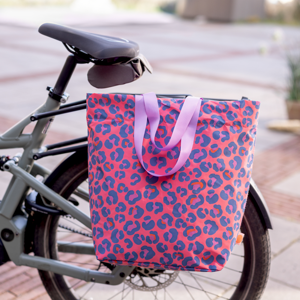 Eine rosa Fahrradtasche mit Leopardenmuster hängt im Freien an einem Fahrrad.