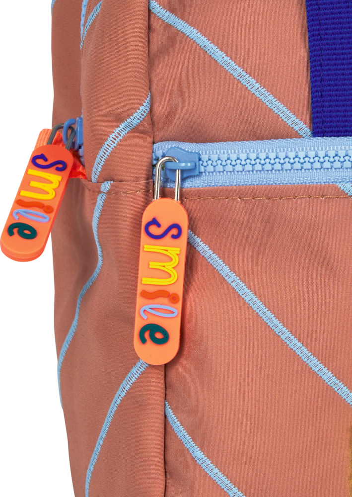 Nahaufnahme eines pfirsichfarbenen Rucksacks mit blauem Reißverschluss und orangefarbenen Zippern, Aufschrift smile in bunten Buchstaben.