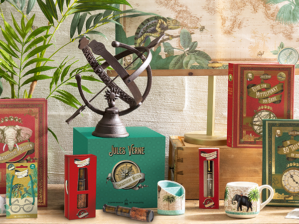 Verschiedene Produkte und Bücher zum Thema Jules Verne in blau, grün und gold, passend mit Karten und Pflanzen im Hintergrund drapiert.