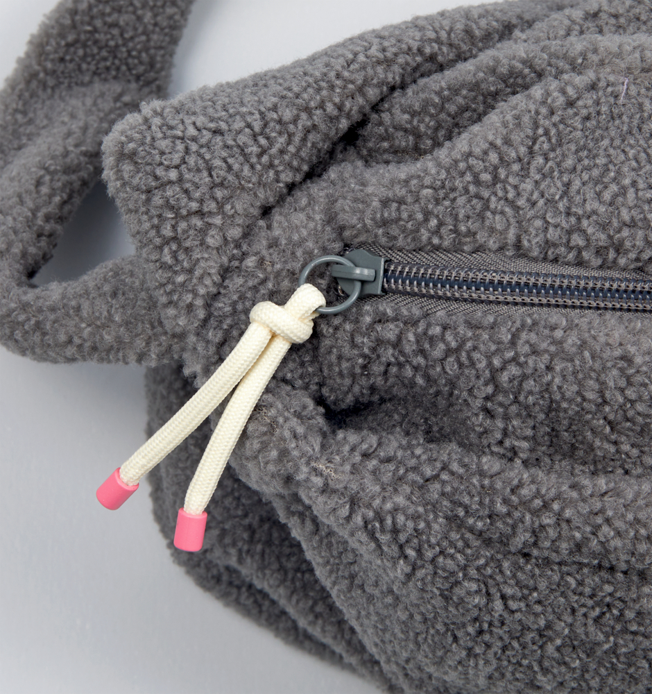 Nahaufnahme einer grauen Fleecetasche mit Reißverschluss und weißen Kordeln mit rosa Spitzen.