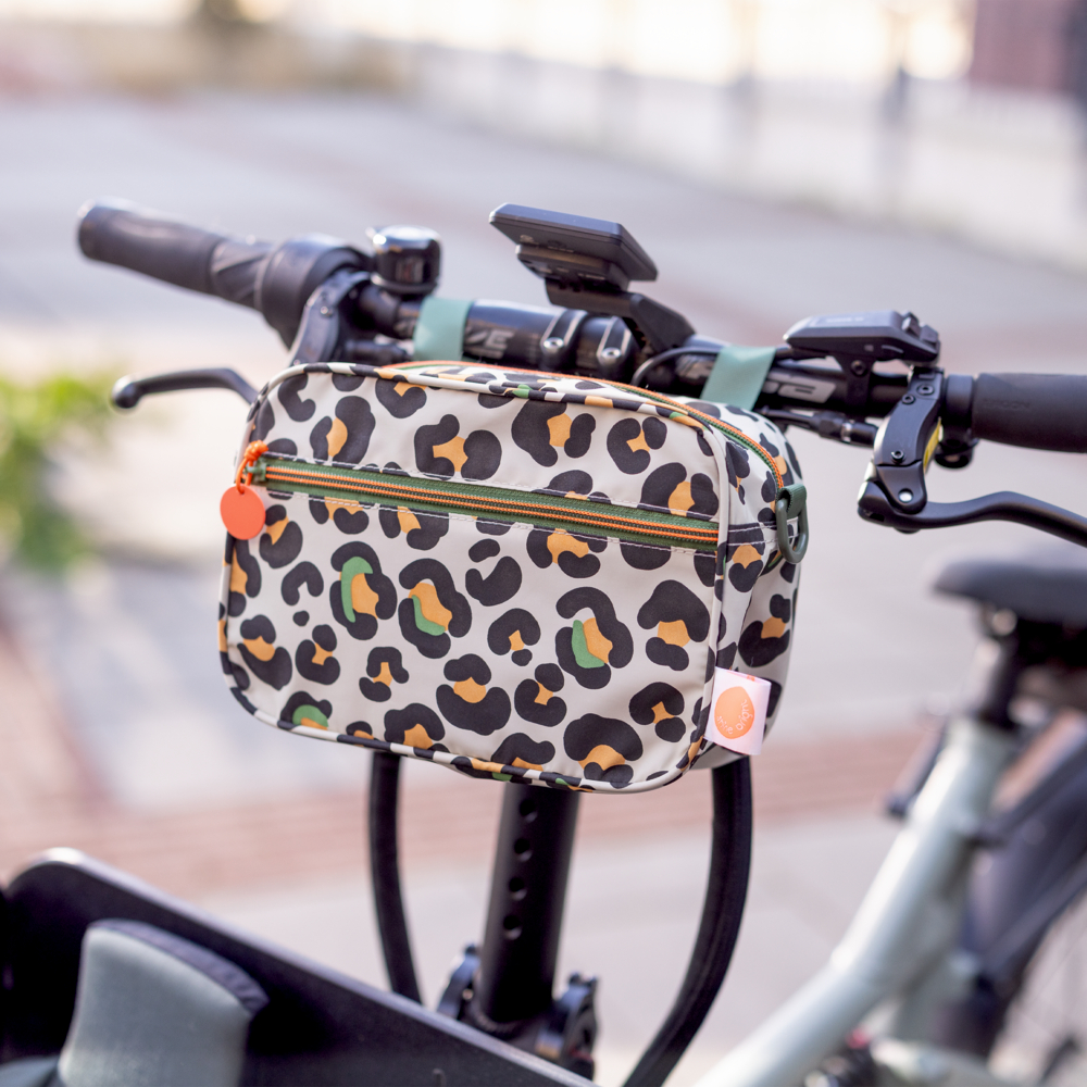 Rechteckiges Täschchen mit mehrfarbigem Leo-Print und Reißverschluss außen an einem Fahrradlenker. 