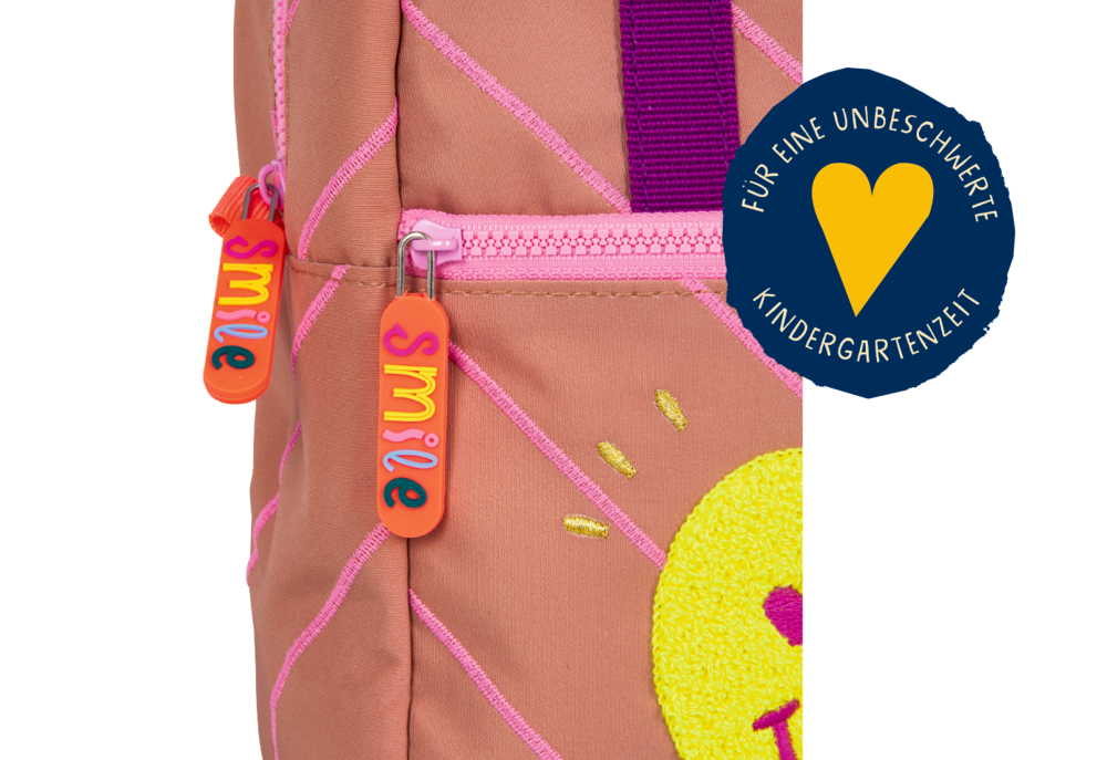 Nahaufnahme eines pinken Rucksacks mit Smile-Reißverschluss und gelbem Herzabzeichen mit Text.