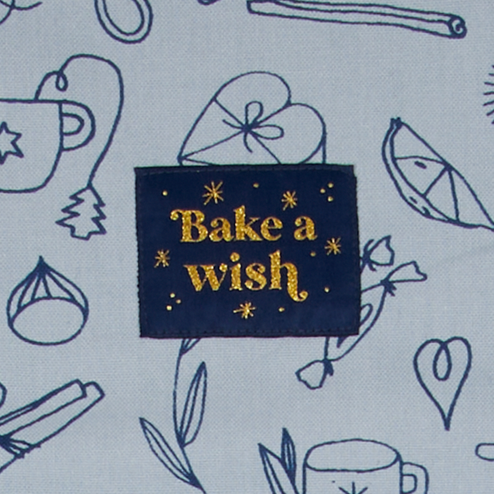 Aufnäher mit „Bake a Wish“ in goldener Schrift und blauen Back-Motiven auf hellblauem Stoff.