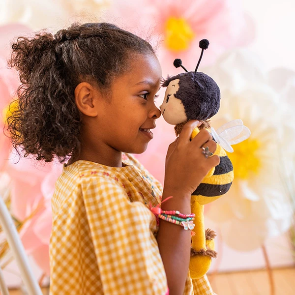 Ein kleines Mädchen lächelt und hält sich eine Plüsch-Biene ganz dicht vor ihr Gesicht