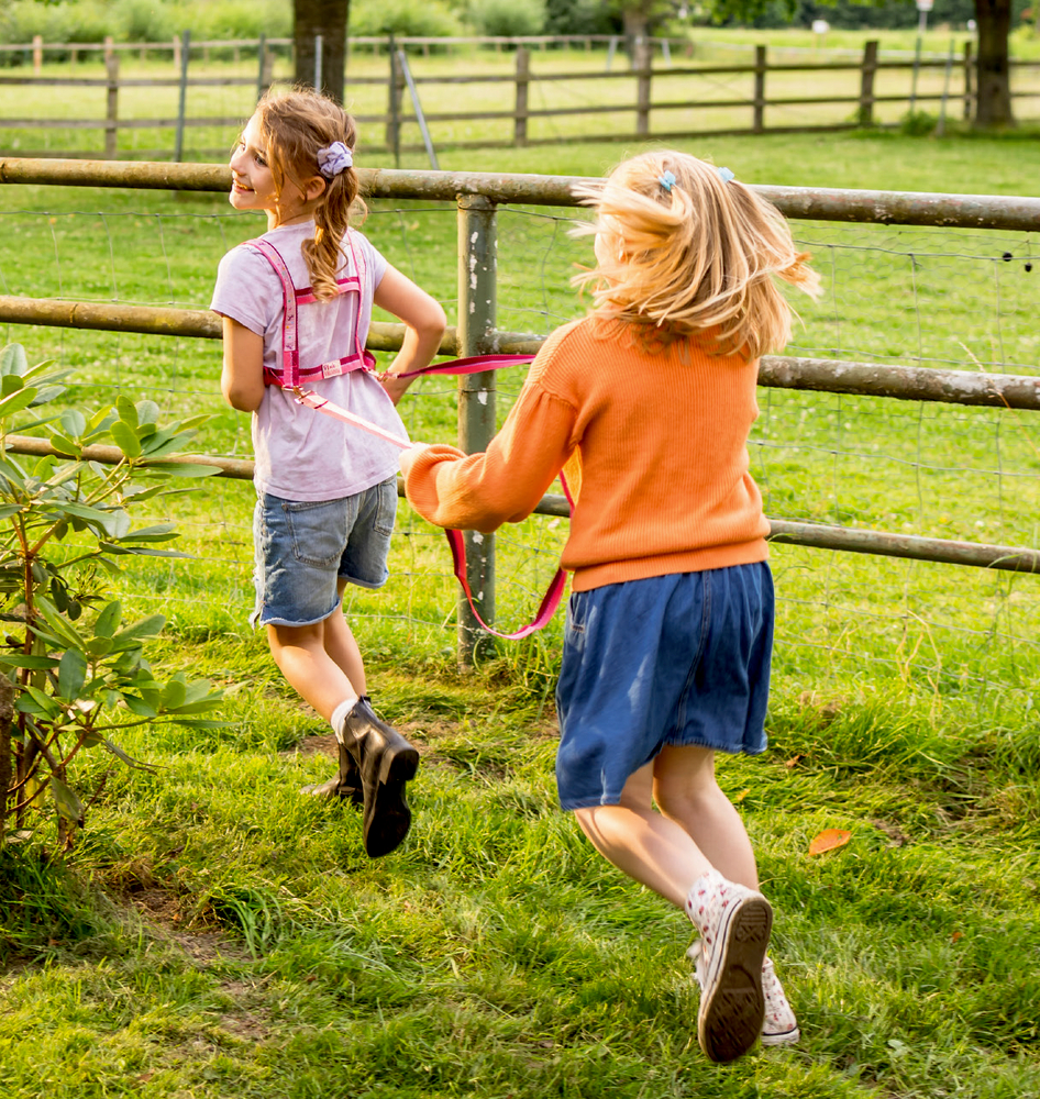 Zwei junge Mädchen rennen und lachen zusammen auf einer Wiese in der Nähe eines Holzzauns und genießen ihre Zeit im Freien.