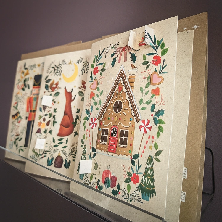 Mehrere weihnachtliche Grußkarten in erdigen Tönen und mit einigen geöffneten Türchen auf einem transparenten Regalbrett.