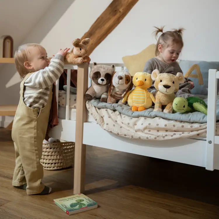 Kleinkinder spielen mit Kuscheltieren und drapieren diese auf einem Bett