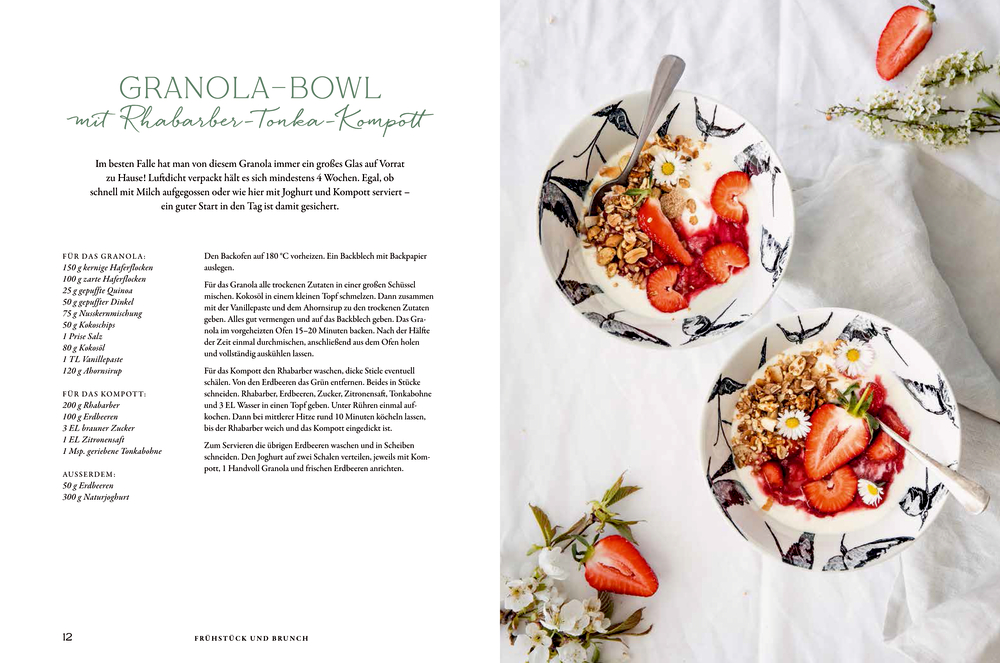 Zwei Joghurtschalen mit Granola, Erdbeeren und Gänseblümchen auf einem weißen, mit Blüten dekorierten Tisch. Links daneben Text.