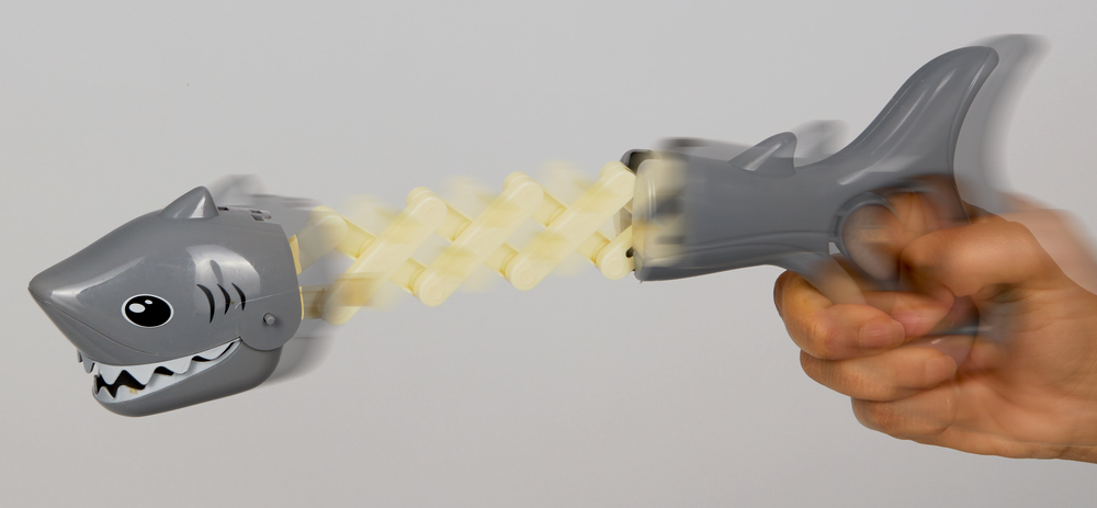 Eine Hand drückt auf einen Hai-Greifer, so dass sich der Haikörper ausfährt und der Hai schnappt.