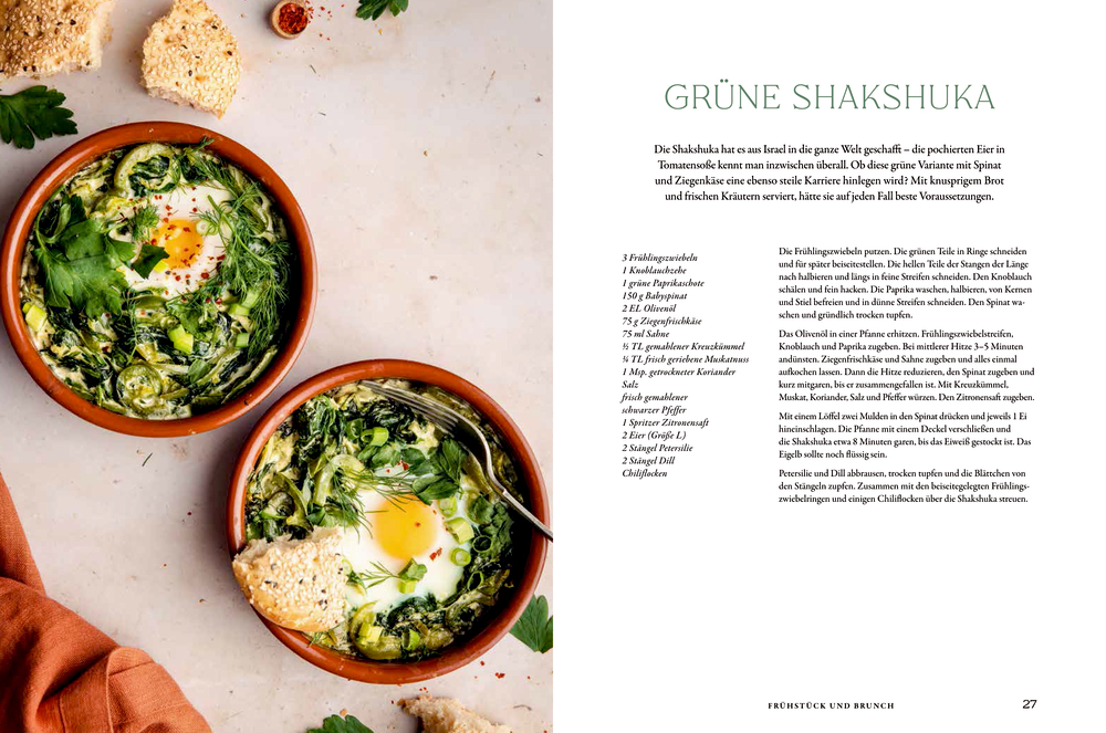 Zwei Schüsseln grünes Shakshuka mit Eiern, Kräutern und Brotchips auf einem weißen Tisch neben einer Rezeptseite.