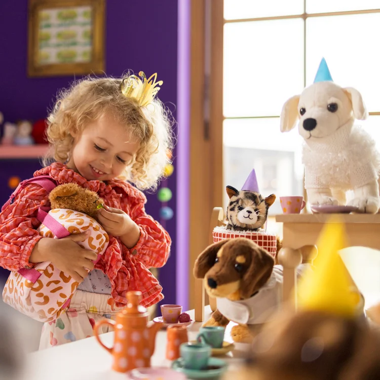 Kleines lockiges Mädchen mit Plüschtieren und Spielgeschirr
