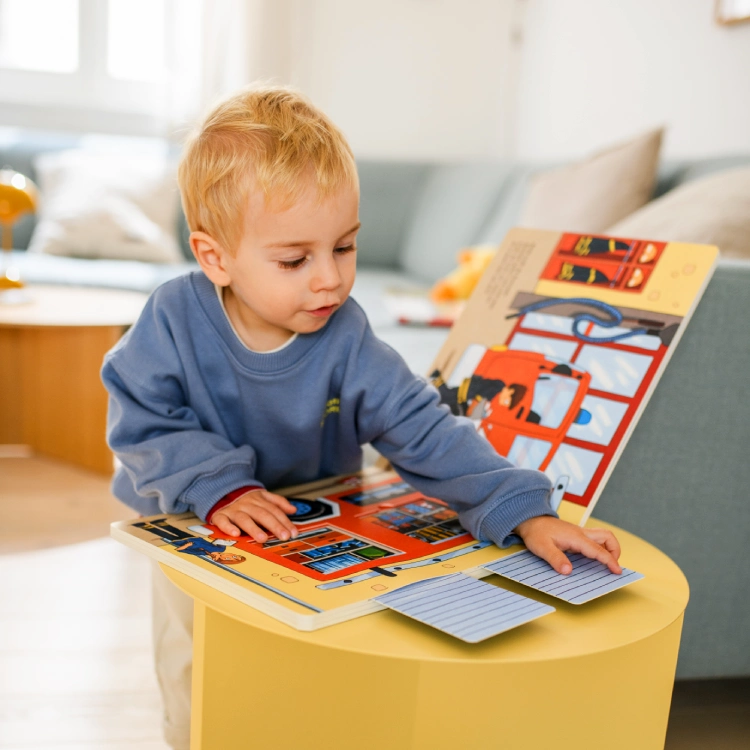 Kleinkind mit interaktivem Pappbilderbuch Kleiner Junge probiert die Klappen eines Pappbilderbuchs aus.