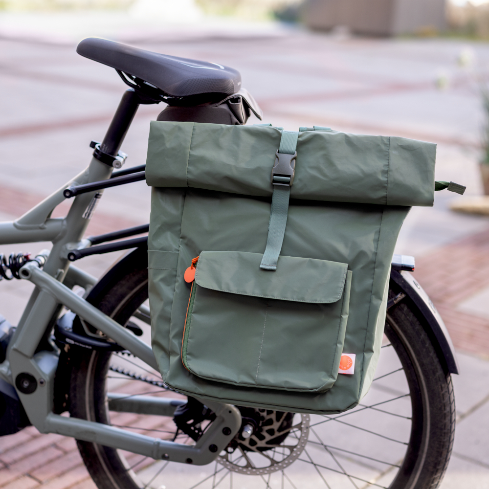 Olivgrüner Rucksack zum Einrollen mit Fronttasche, montiert am Gepäckträger eines Fahrrads.