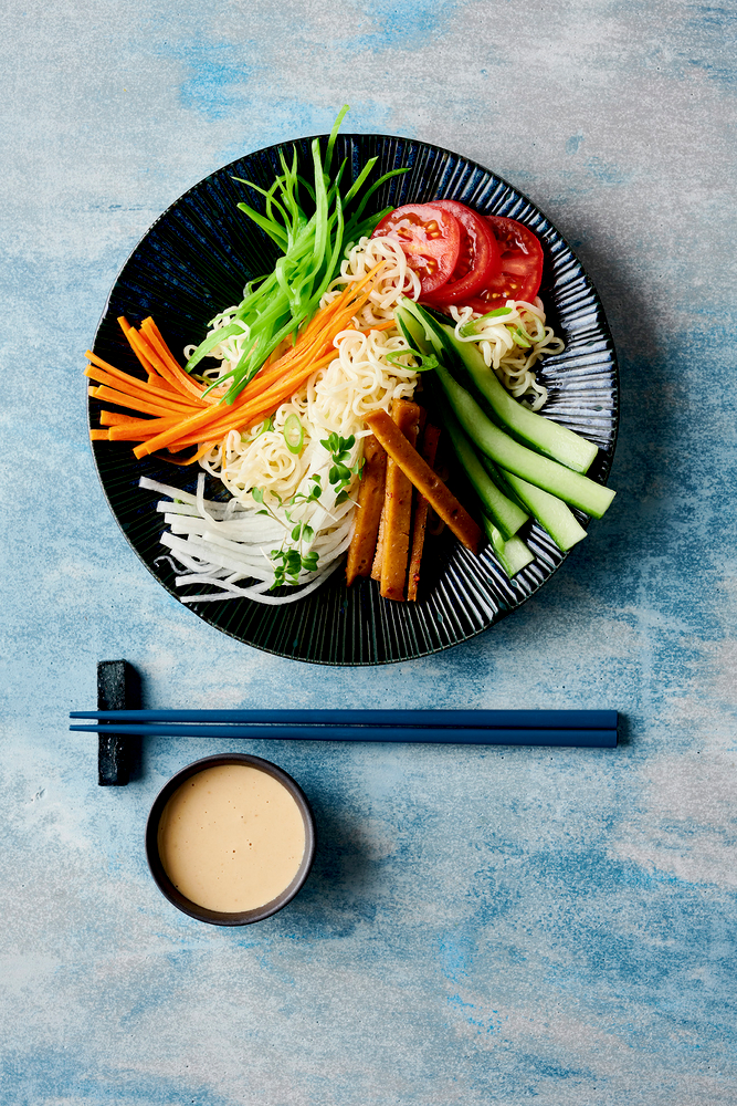 Ramen mit geschnittenem Gemüse, Tofu und Essstäbchen, serviert mit einer Tasse Dip-Sauce.