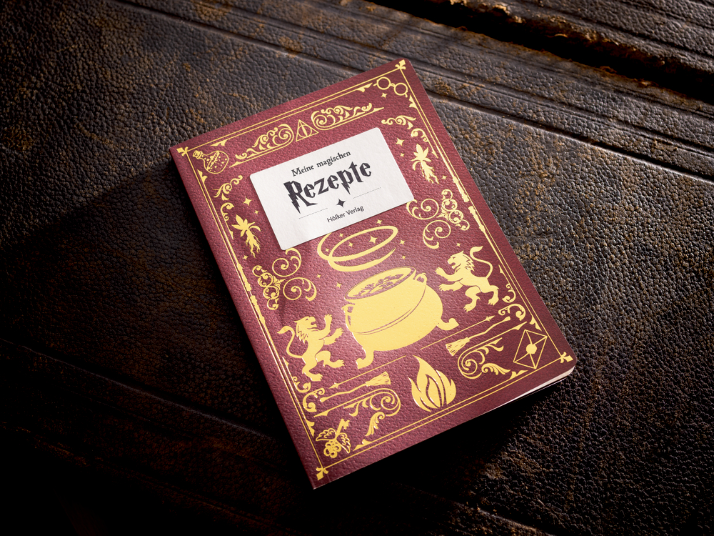 Ein rotes Rezeptbuch mit goldenen Motiven liegt auf einer dunklen Holzoberfläche.