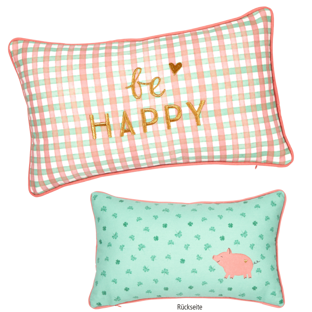 Rechteckige Kissen: eines mit dem Karomuster „be HAPPY“, das andere mit Kleeblättern und der Abbildung eines rosa Schweins.
