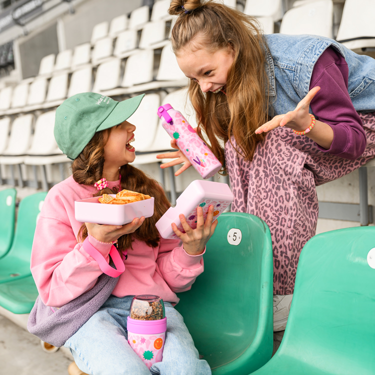 Zwei lachende Mädchen mit stylischer Brotdose und Trinkflasche.
