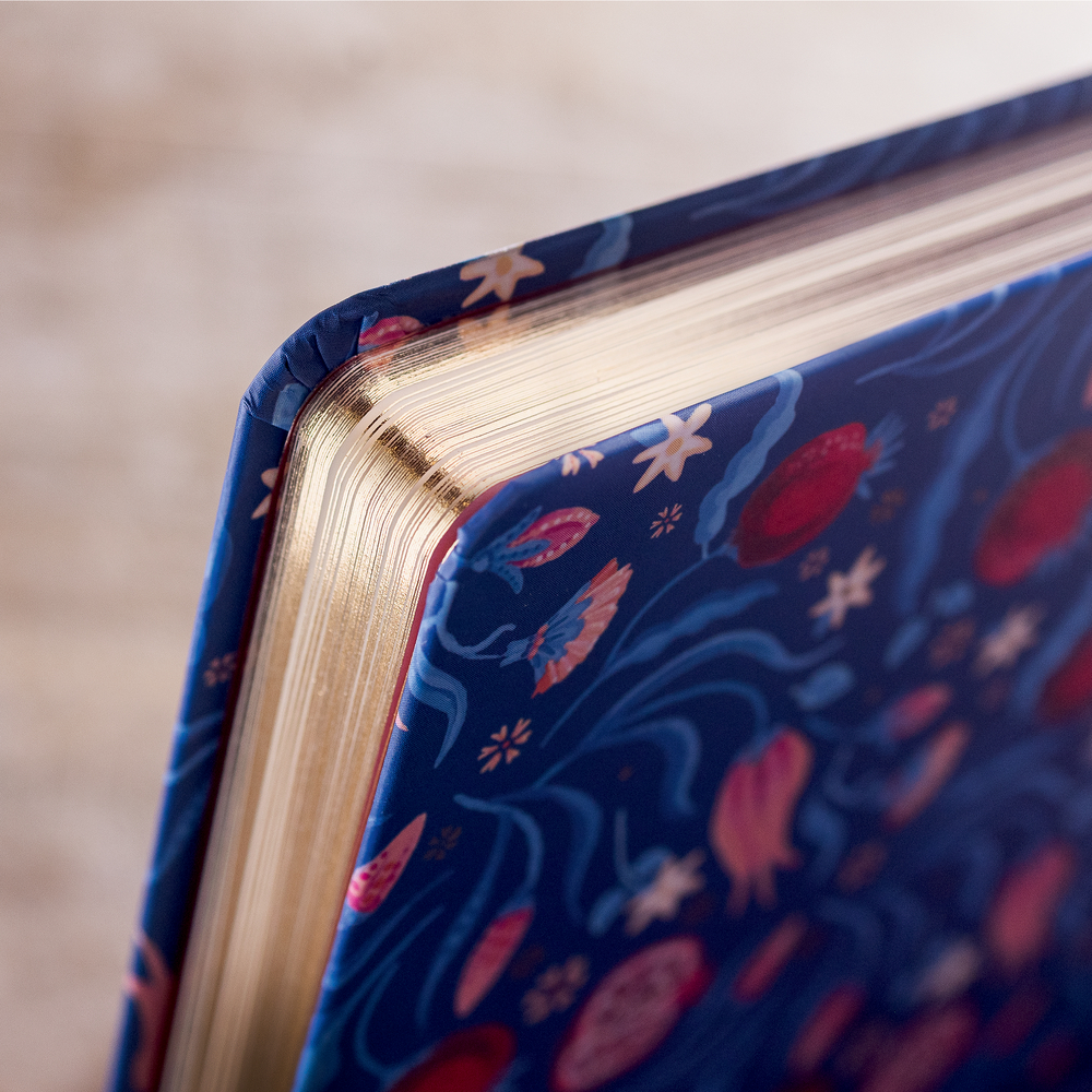 Nahaufnahme einer Buchecke mit blauem, floral gemustertem Einband und goldfarbenem Schnitt.