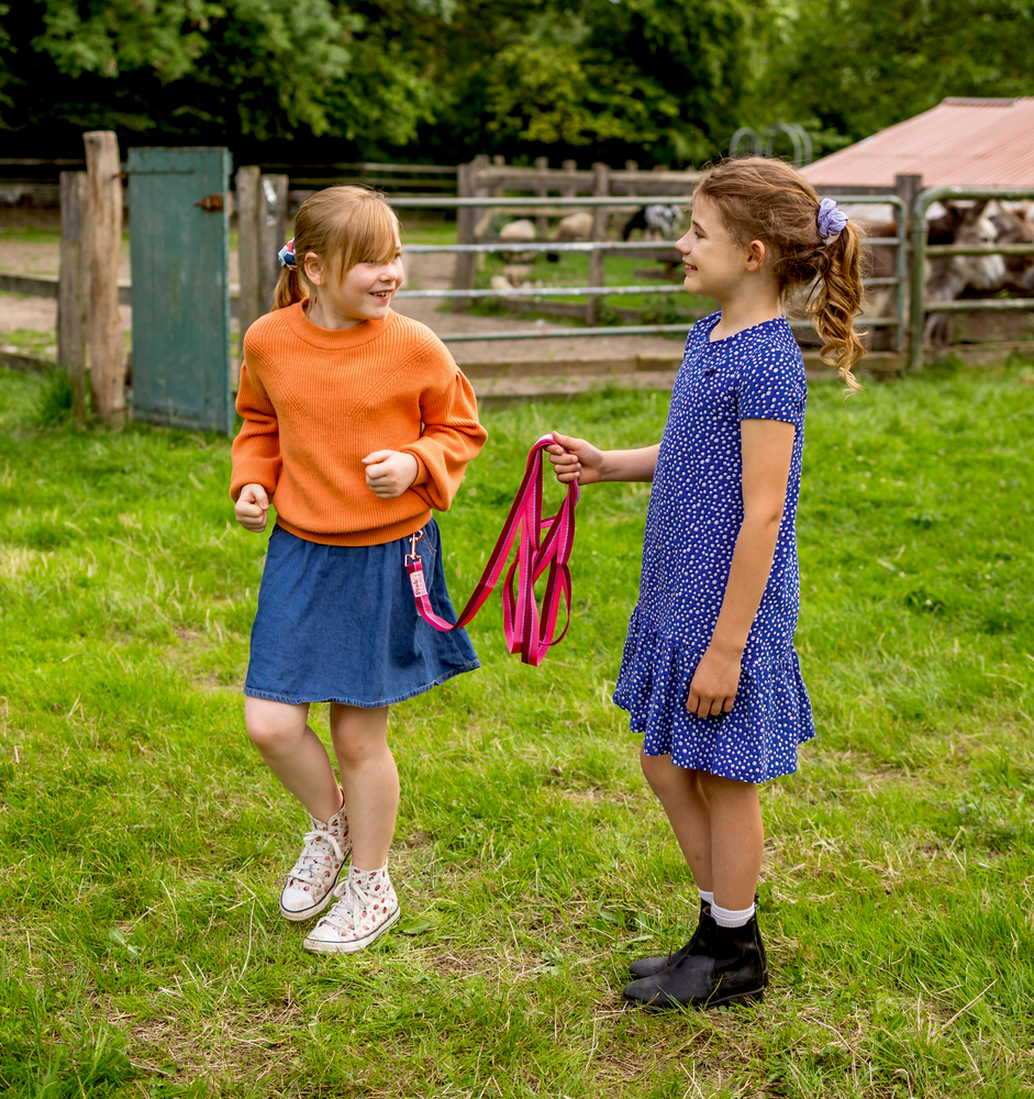 Zwei junge Mädchen lächeln und spielen zusammen auf dem Rasen, eines von ihnen hält eine rosa Leine.