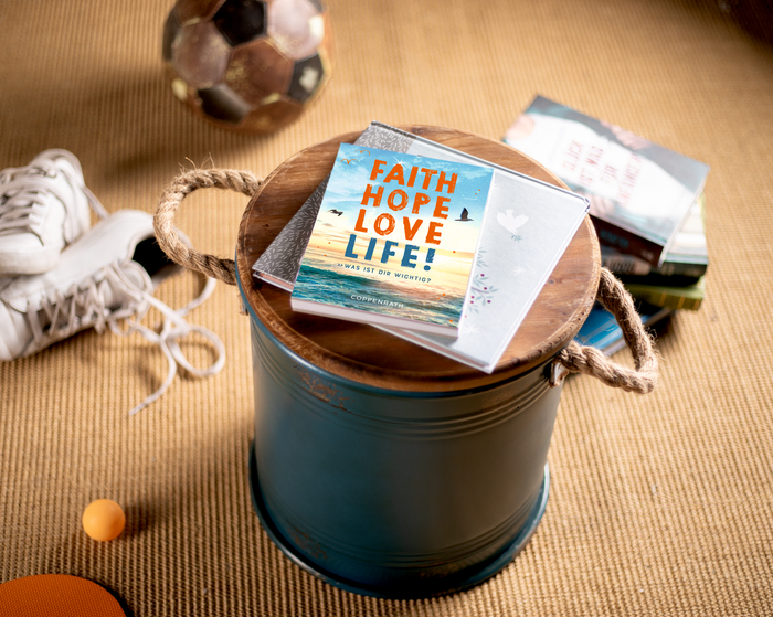 Cover des Coppenrath christlichen Titels Faith, Hope, Love, Life! auf einem runden Hocker und Sportgeräten im Hintergrund