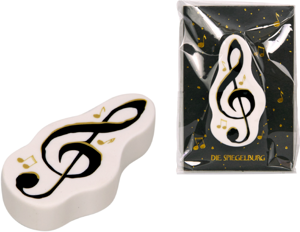Ein weißer Radiergummi in Notenform mit schwarzem Violinschlüssel und goldenen Noten, daneben die Verpackung.