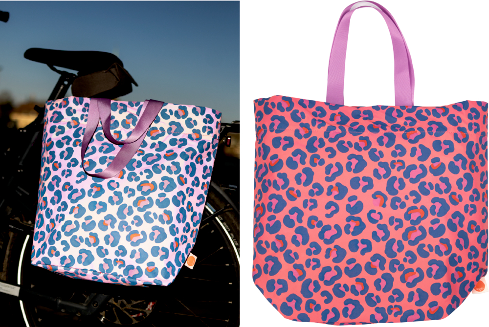 Zwei Tragetaschen mit Leopardenmuster – blau/weiß auf einem Fahrrad und rosa mit violetten Griffen – stehen nebeneinander.