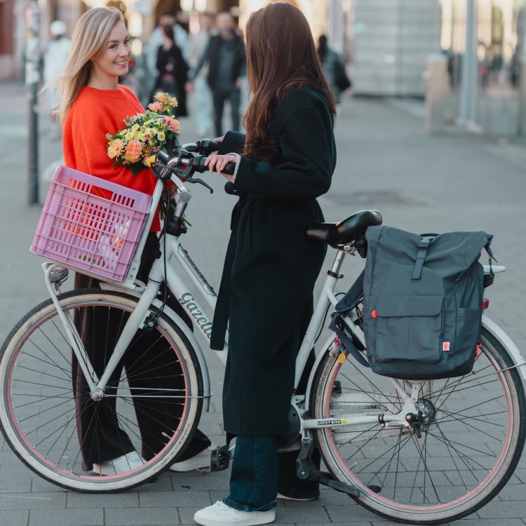 Zwei Frauen mit Fahrrad und Fahrradtasche auf einem städtischen Platz