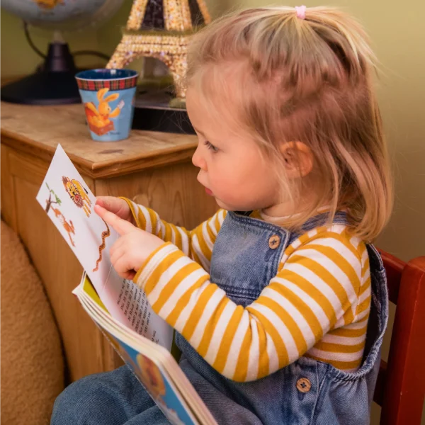 Kleines Mädchen betrachtet ein Bilderbuch und zeigt auf etwas im Buch.