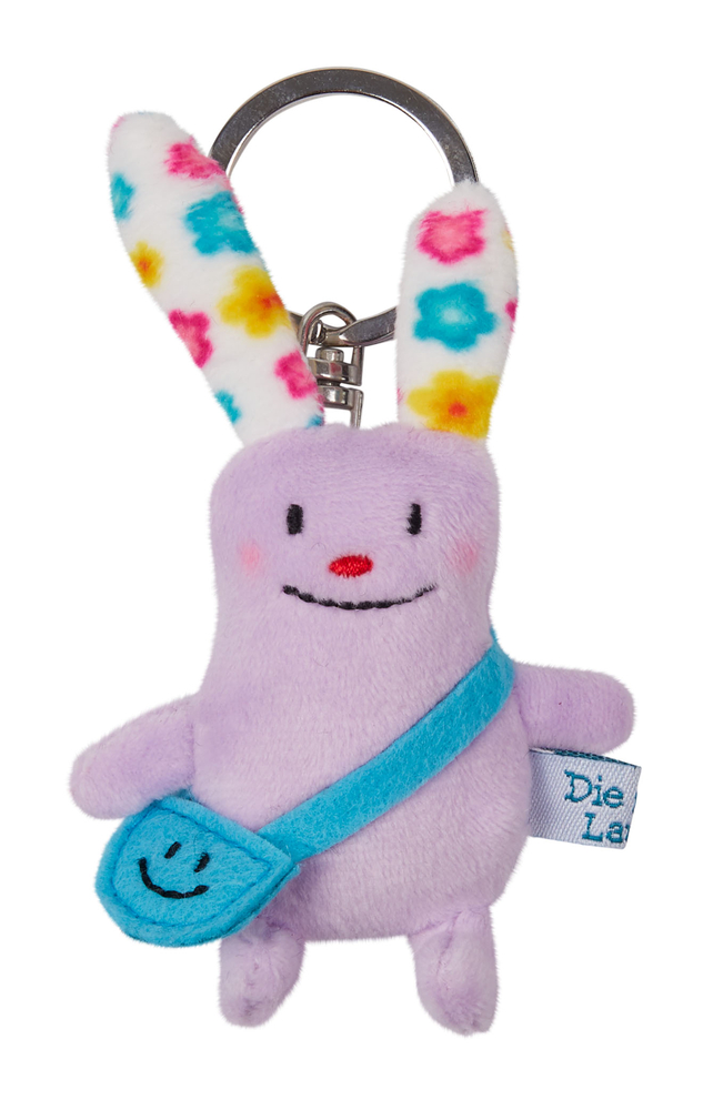 Schlüsselanhänger Die gute Laune (Das kleine Glück) Lila Plüschfigur-Schlüsselanhänger mit bunten Ohren, blauer Tasche und einem lächelnden Gesicht.