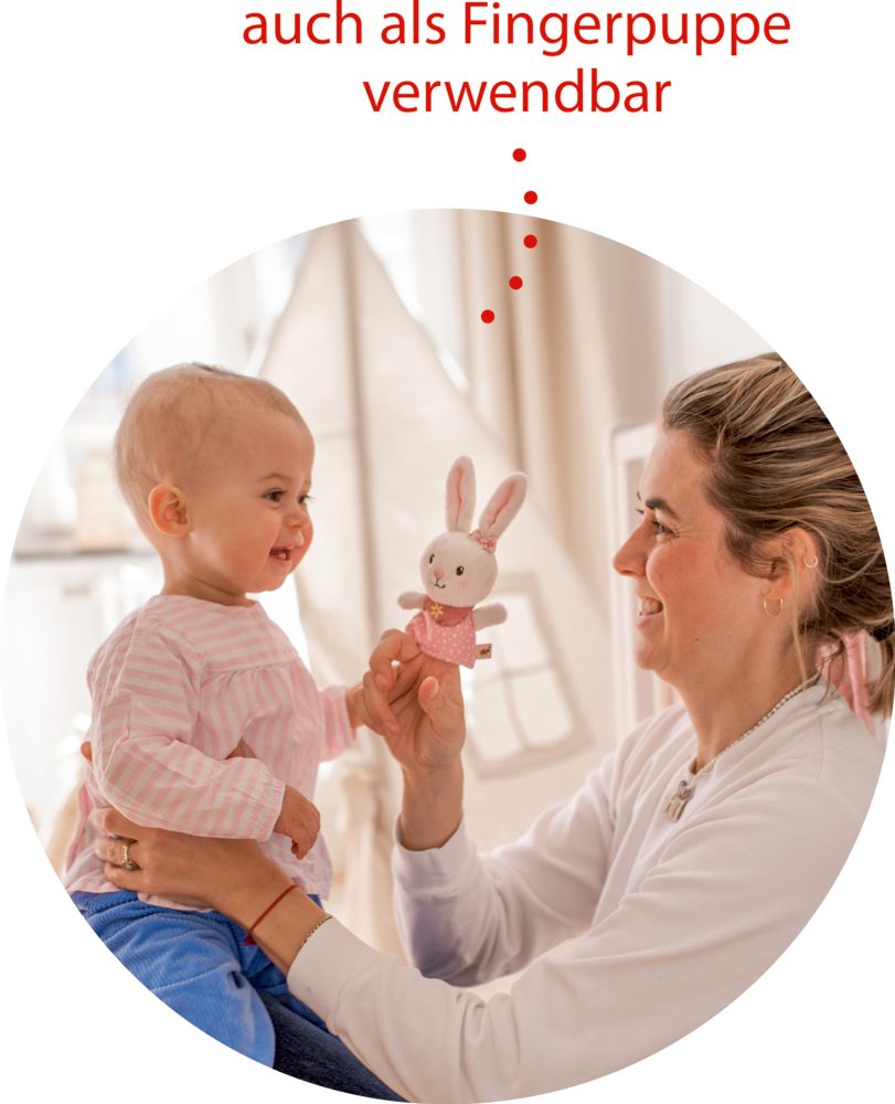 Eine Frau lächelt, als sie einem glücklichen Baby in einem gemütlichen Zimmer eine Hasen-Fingerpuppe zeigt.