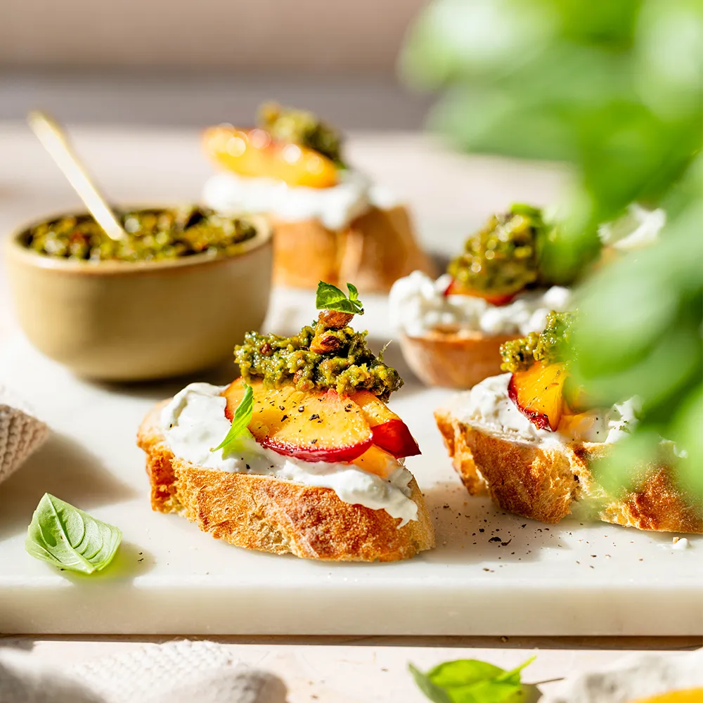 Geröstetes Baguette mit Burrata, gebratenen Pfirsichspalten und Pistazienpesto