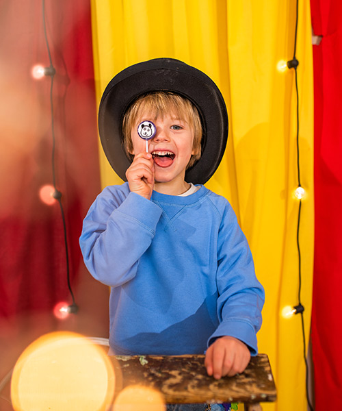 Lachender Junge mit Zylinder und Zauberartikel in Zirkus-Umgebung.