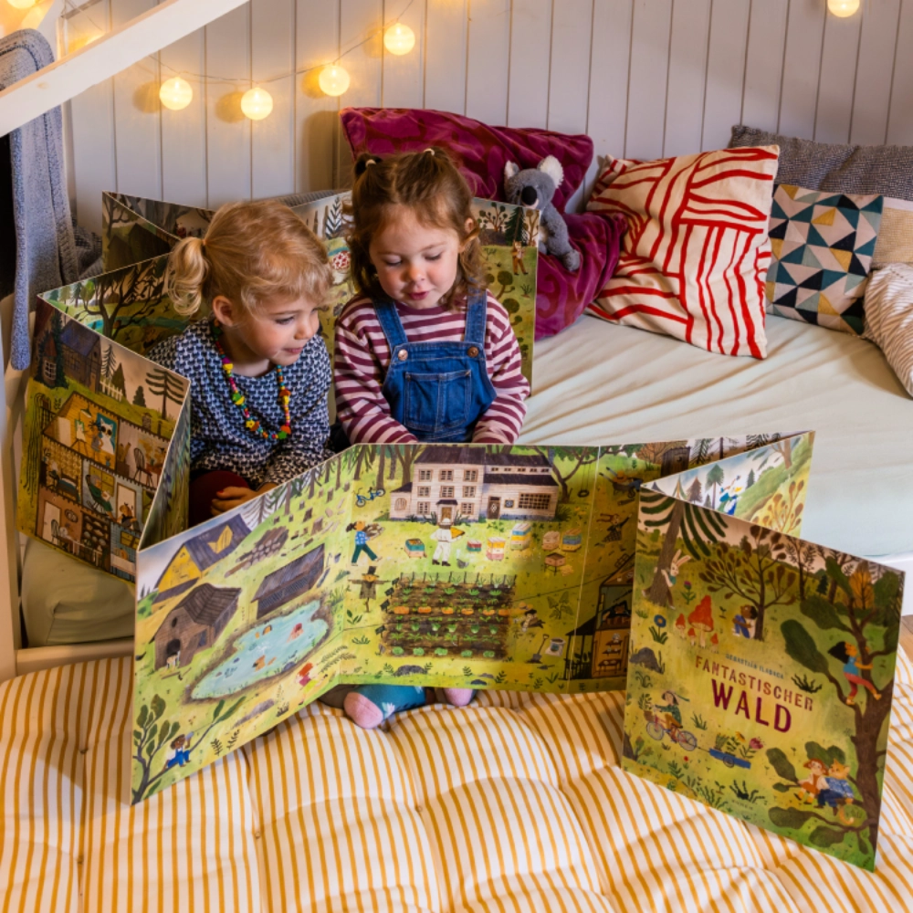 Banner Aufklapbilderbuch Fantastischer Wald zwei kleine Mädchen betrachten ein großes aufgeschlagenes Leporellobuch in gemütlicher Umgebung.