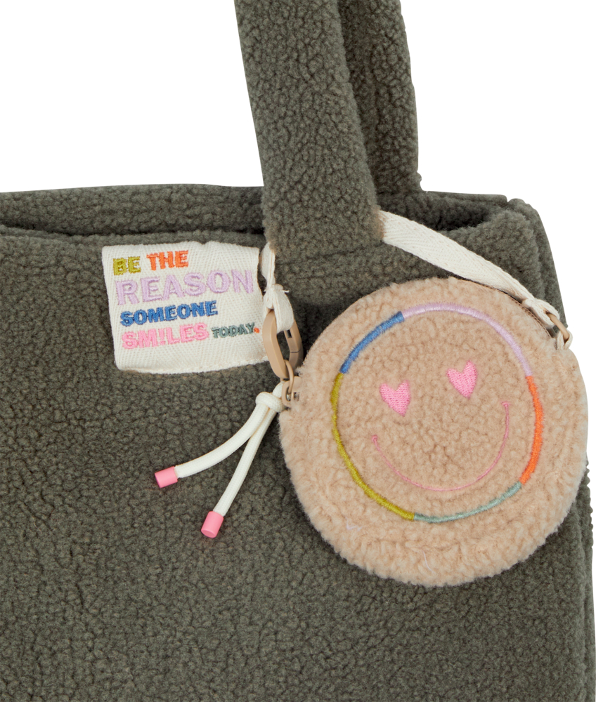 Nahaufnahme einer flauschigen grauen Einkaufstasche mit einem runden Smiley-Anhänger und einem bunten Motivationsanhänger.