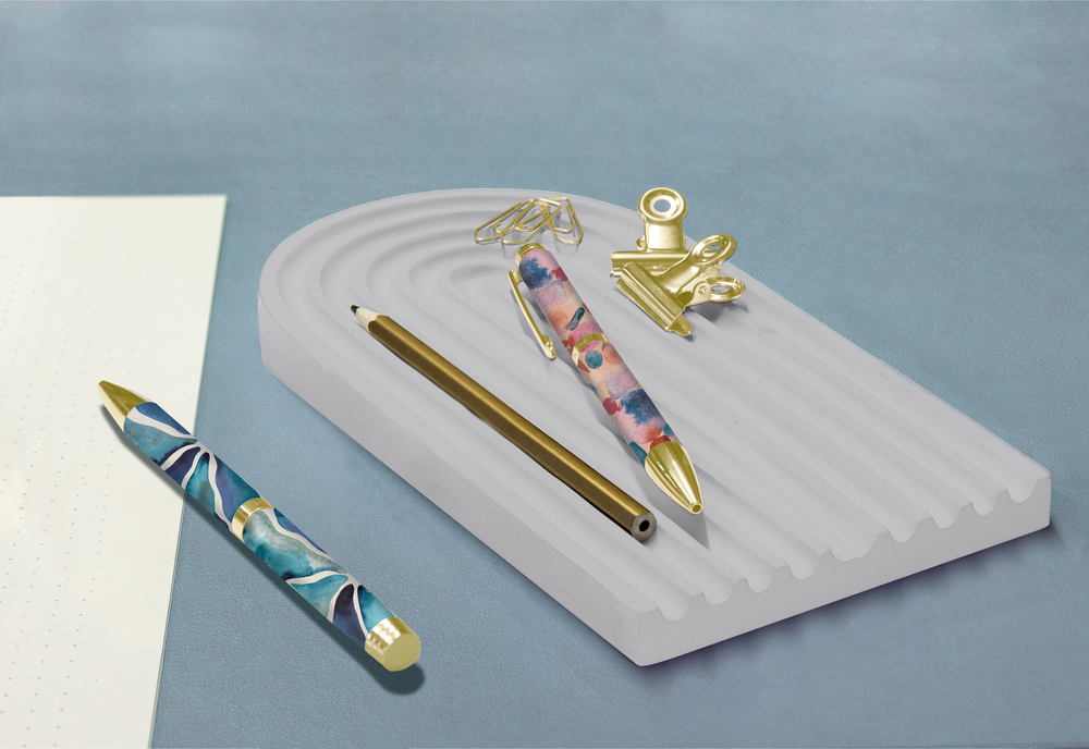 Zwei bunte Stifte, goldene Büroklammern und goldener Bleistift auf einem Schreibtisch-Organizer neben gepunktetem Papier.