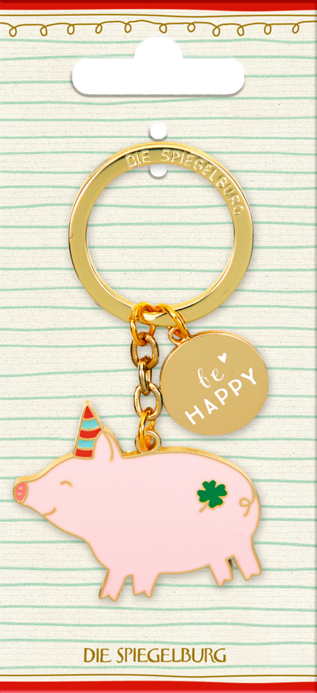 Goldener Schlüsselanhänger mit rosa Schwein, grünem Kleeblatt und rundem „Be HAPPY“-Schild auf linierter Pappe.