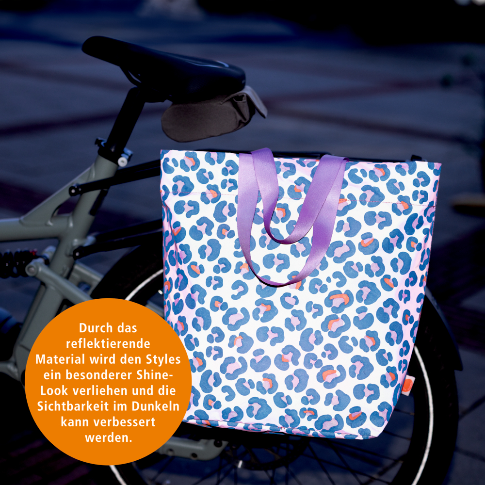 Eine bunte, reflektierende Tasche mit lilafarbenen Henkeln am Fahrrad erhöht die Sichtbarkeit im Dunkeln.