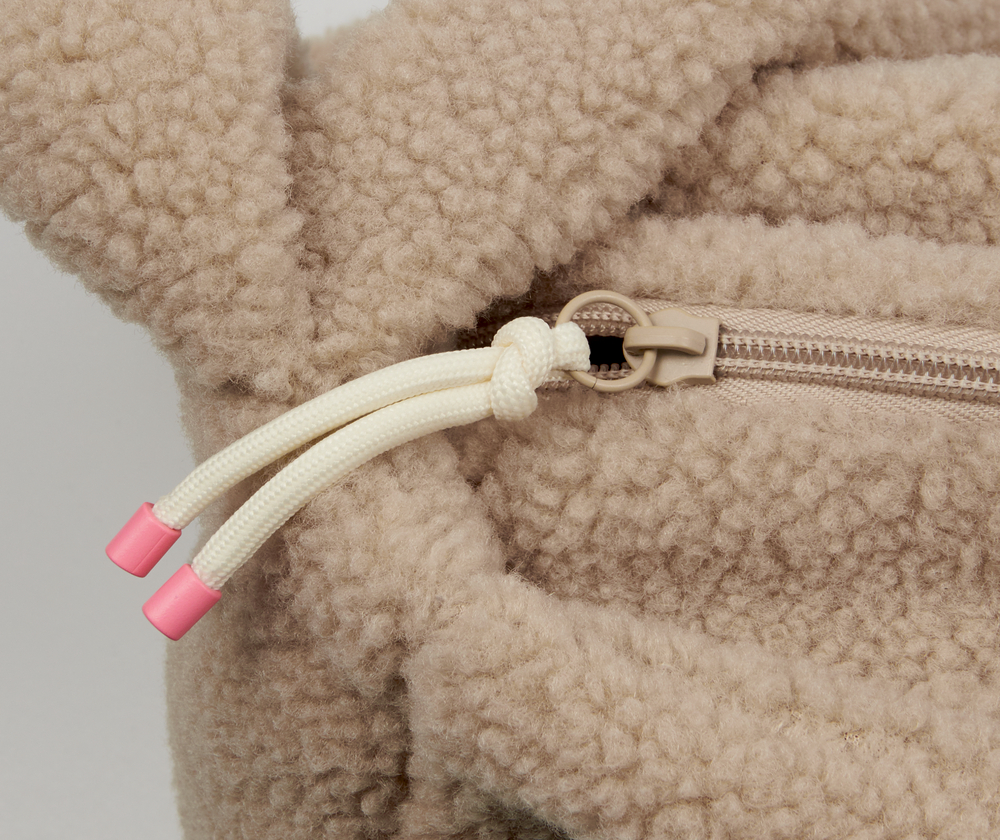 Nahaufnahme einer hellbraunen Fleecetasche mit Reißverschluss und weißen Kordeln mit rosafarbenen Plastikenden.
