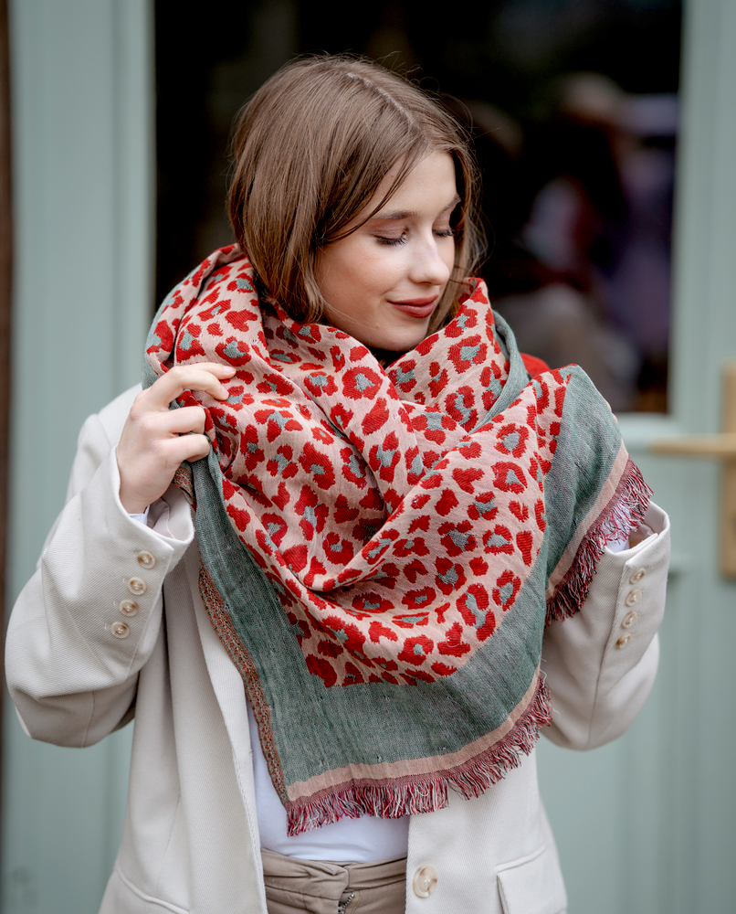 Frau in beigem Mantel und rot-grauem Schal mit Leopardenmuster steht an einer Tür.