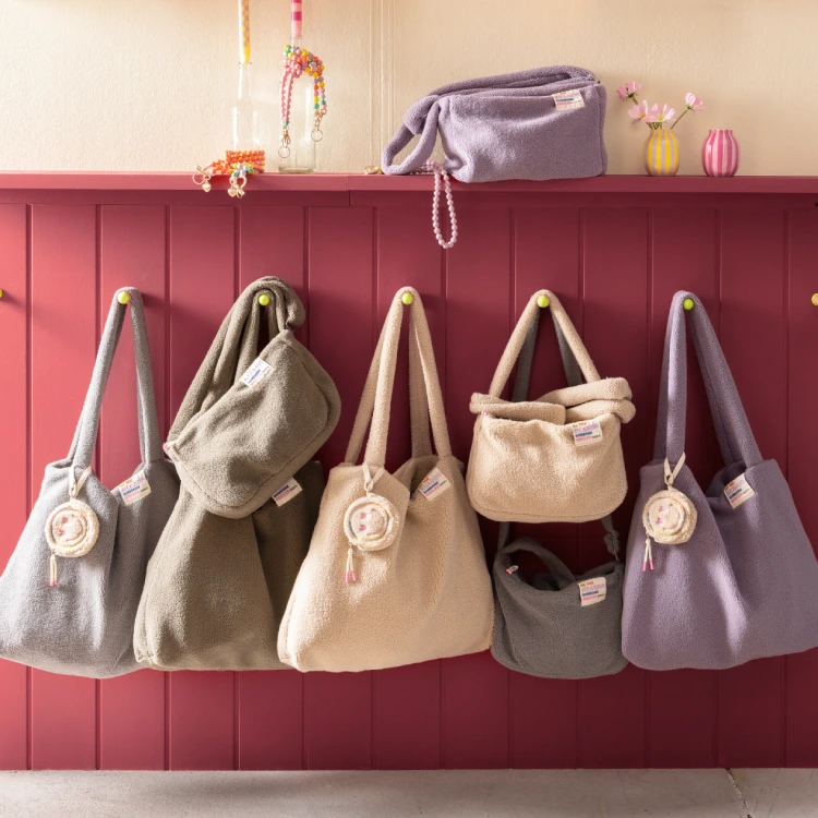 Mehrere Taschen in Teddy-Optik und mit verschiedenen Pastellfarben hängen an einer Hakenwand.