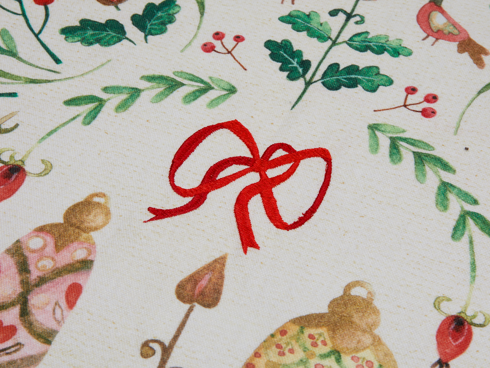 Eine rote Schleife sitzt inmitten von festlichem Grün und Weihnachts-Ornamenten auf cremefarbenem Stoff.