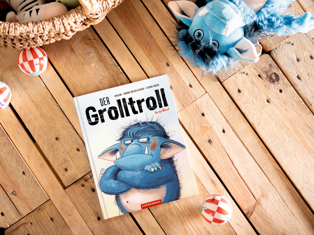 Der Grolltroll Kinderbuch auf einem Holzboden, umgeben von Plüschtieren und bunten Bällen.