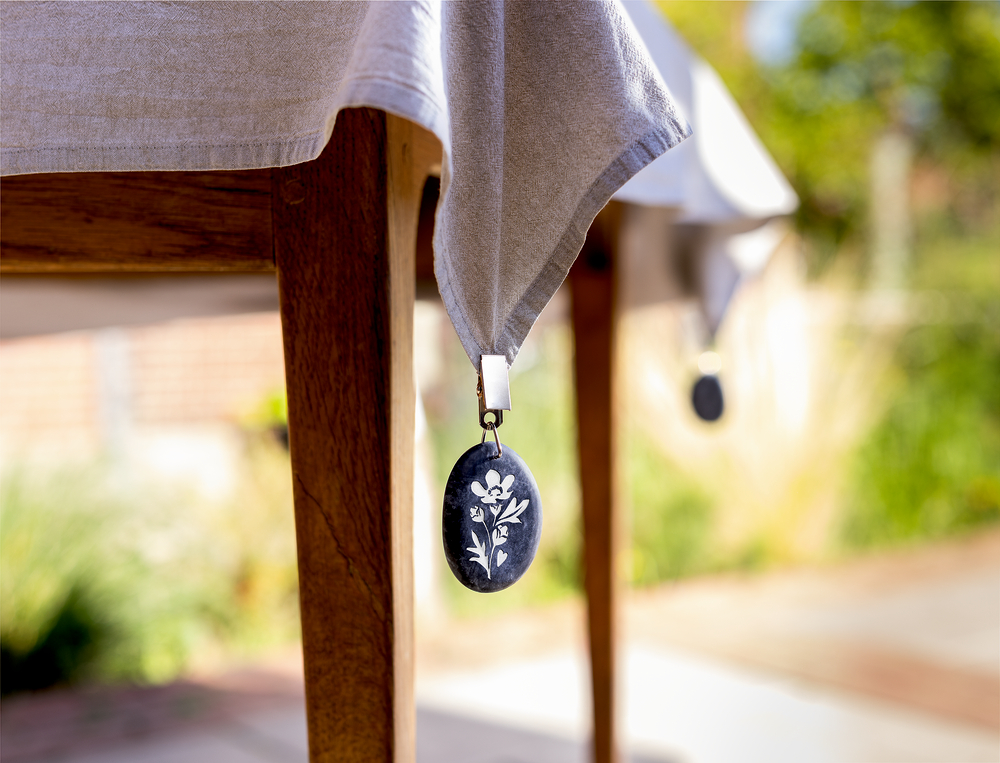 Nahaufnahme eines Tisches mit grauem Tuch, beschwert mit einem dunkelblauen, runden Gewicht mit weißem Blumendesign.