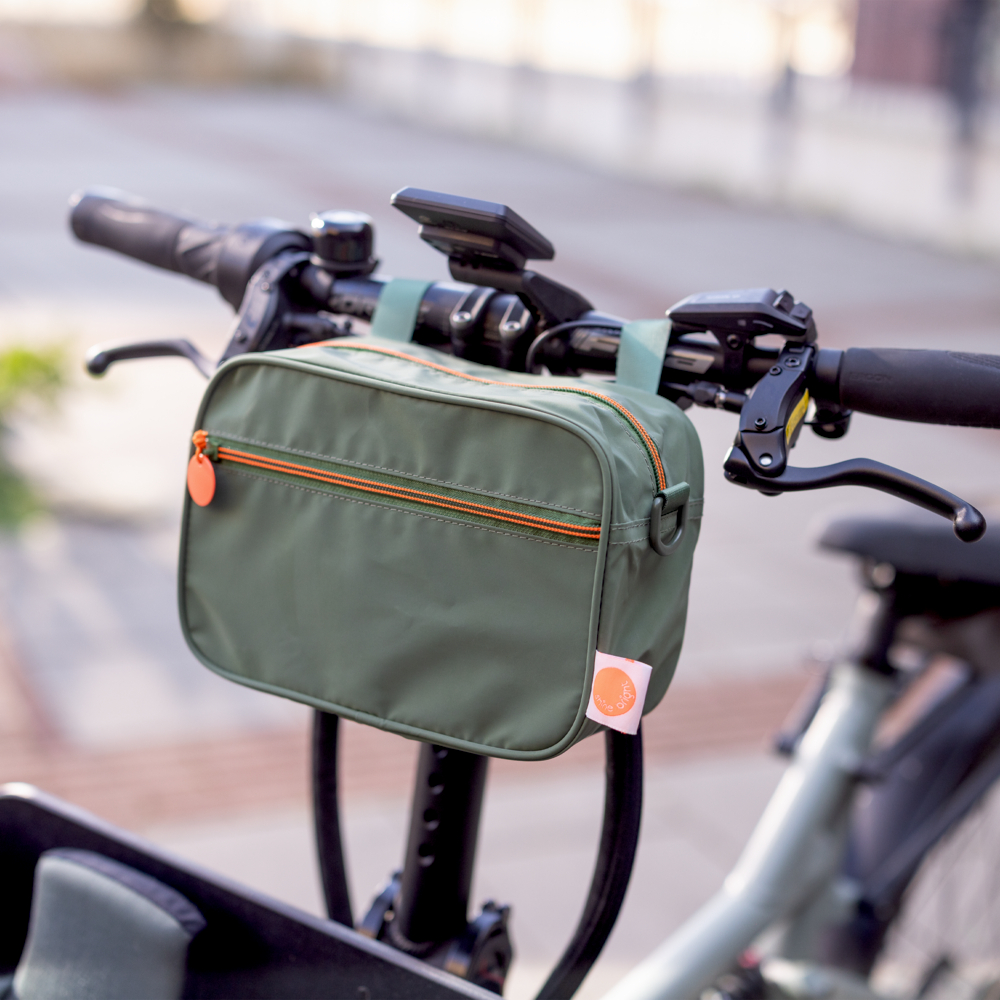 Rechteckiges, olivgrünes Täschchen mit orangefarbenem Reißverschluss außen an einem Fahrradlenker. 