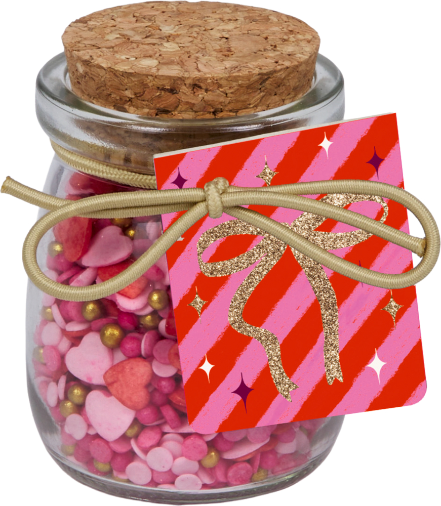 Glas mit Korkdeckel, gefüllt mit rosa und roten Zuckerstreuseln in Herzform, goldfarbene Kordel mit Anhänger in Rot und Pink.