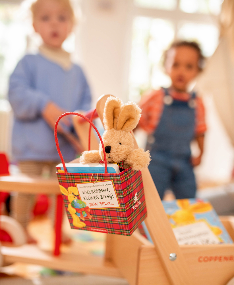 Plüschhase in einem karierten Korb mit einer Notiz und im Hintergrund sind zwei Kinder unscharf zusehen.