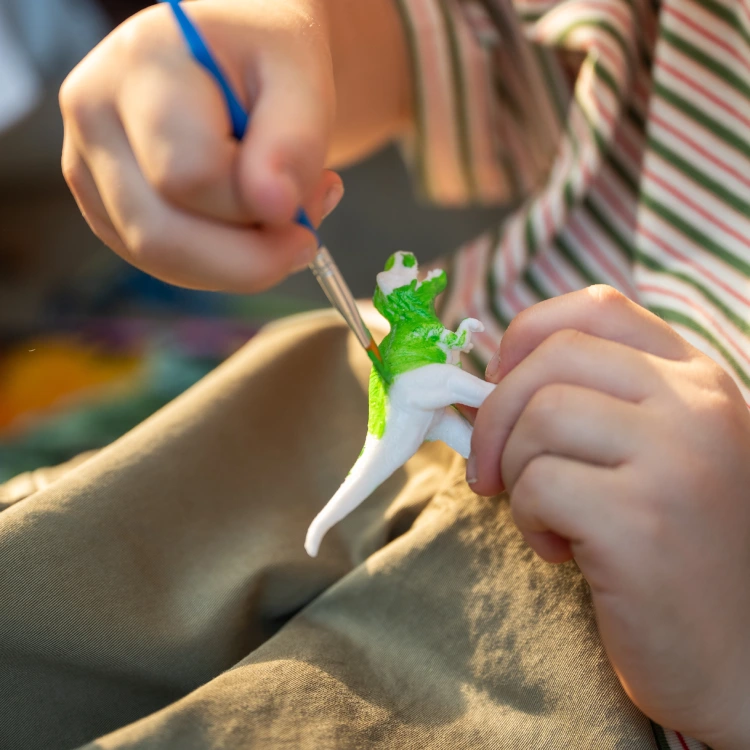 Kinderhand bemalt einen kleinen weißen Gipsdino