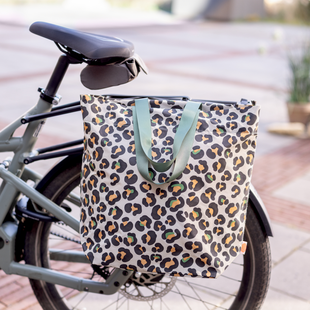 Eine große Fahrradtasche mit Leopardenmuster hängt im Freien am Gepäckträger eines abgestellten Fahrrads.