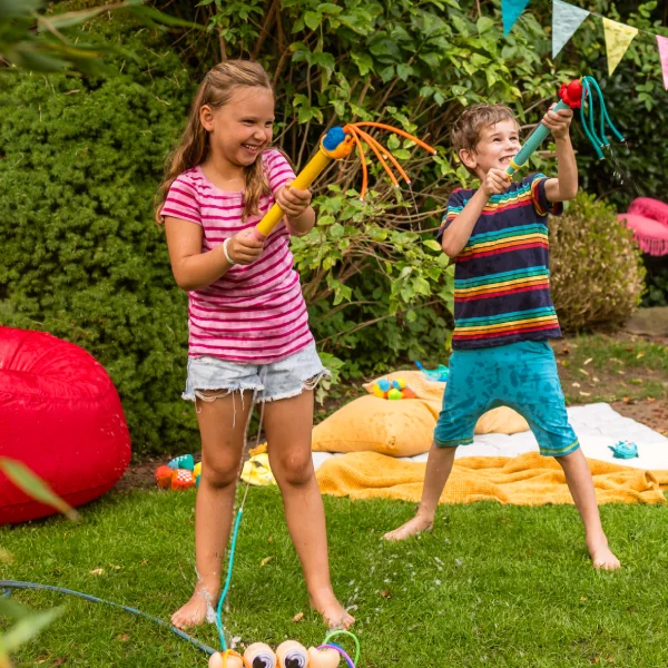 Zwei lachende Kinder auf einer Wiese mit Outdoor-Spielzeug.